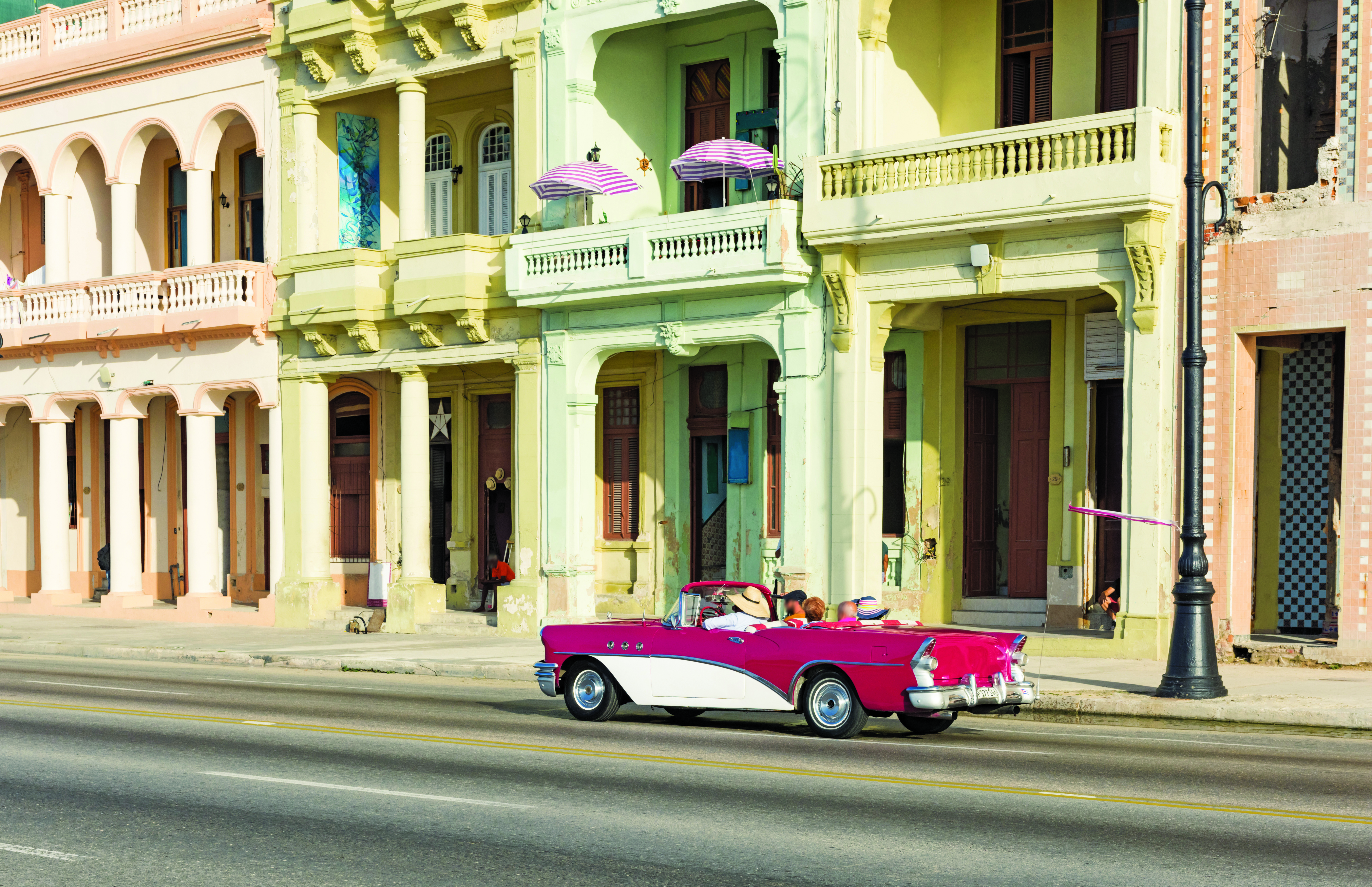 A city street in Cuba with a white row of building, and a fancy red and white car driving in front of it. 