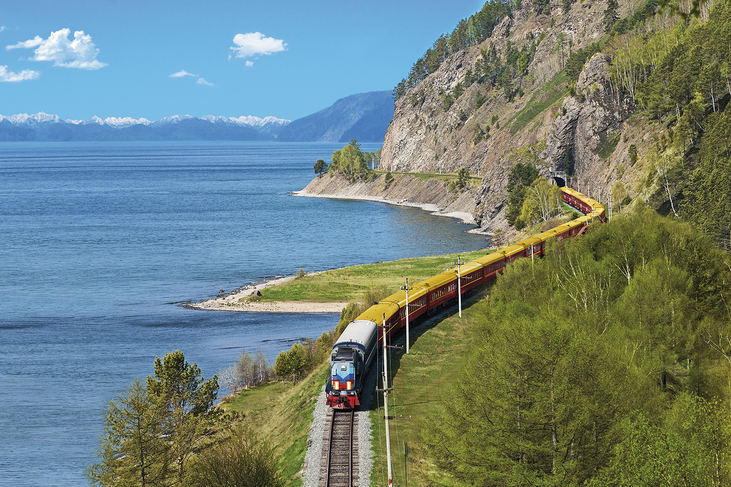 Lake Baikal. Blue lake on the left, a train running on the hillside on the right. 