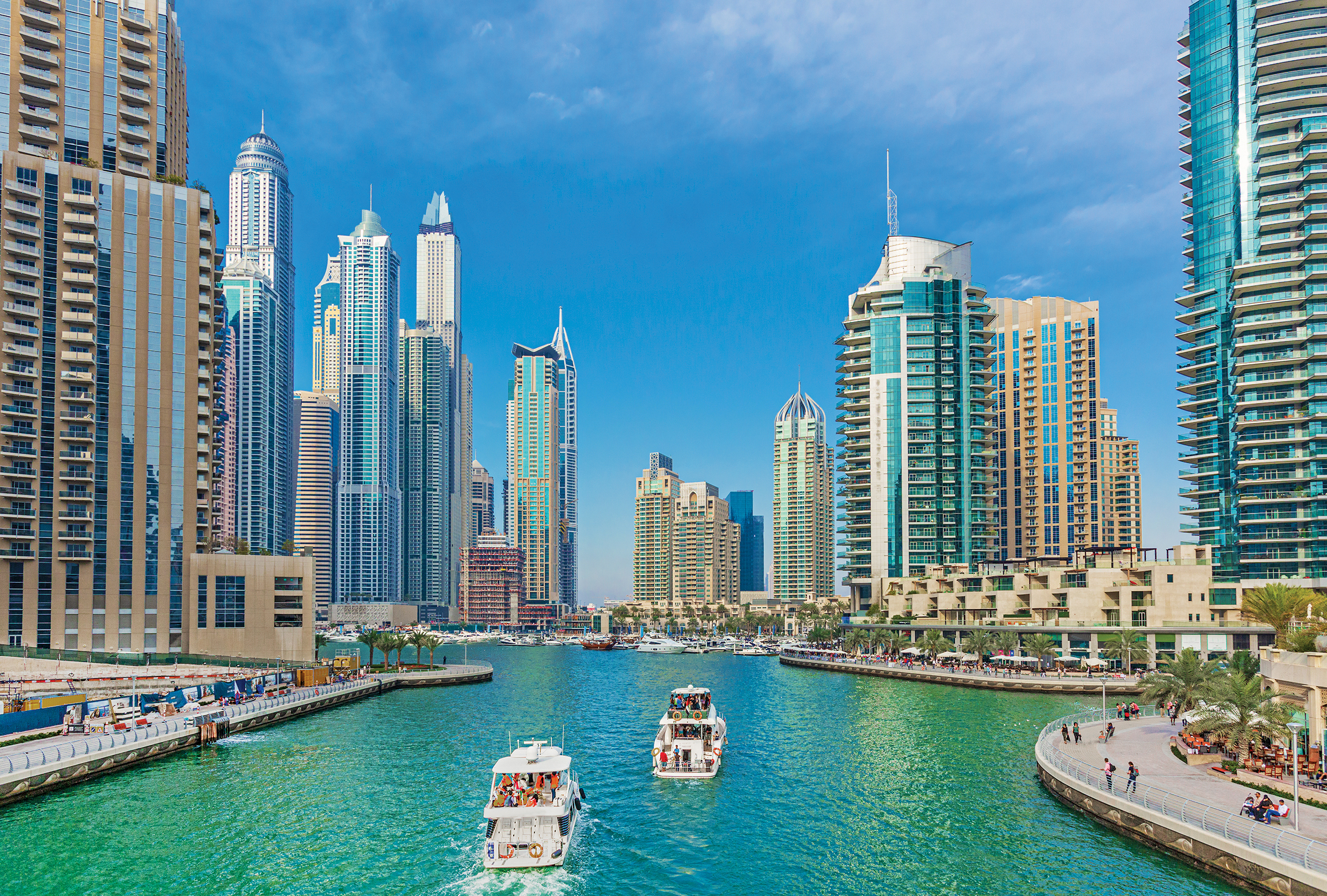 Dubia marina, featuring two boats floating down the canal with large buildings on either side and in front of them. 