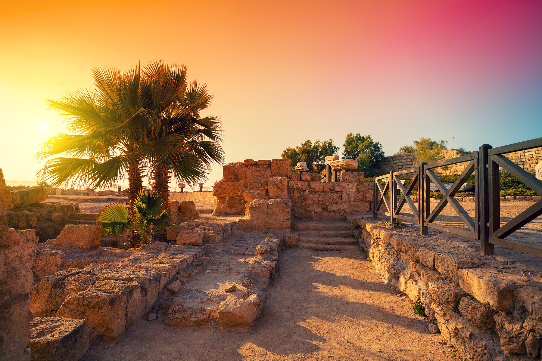 Palm tree on the left, with parts of ancient building viewable, and a beautiful yellow, orange, and red sunset. 