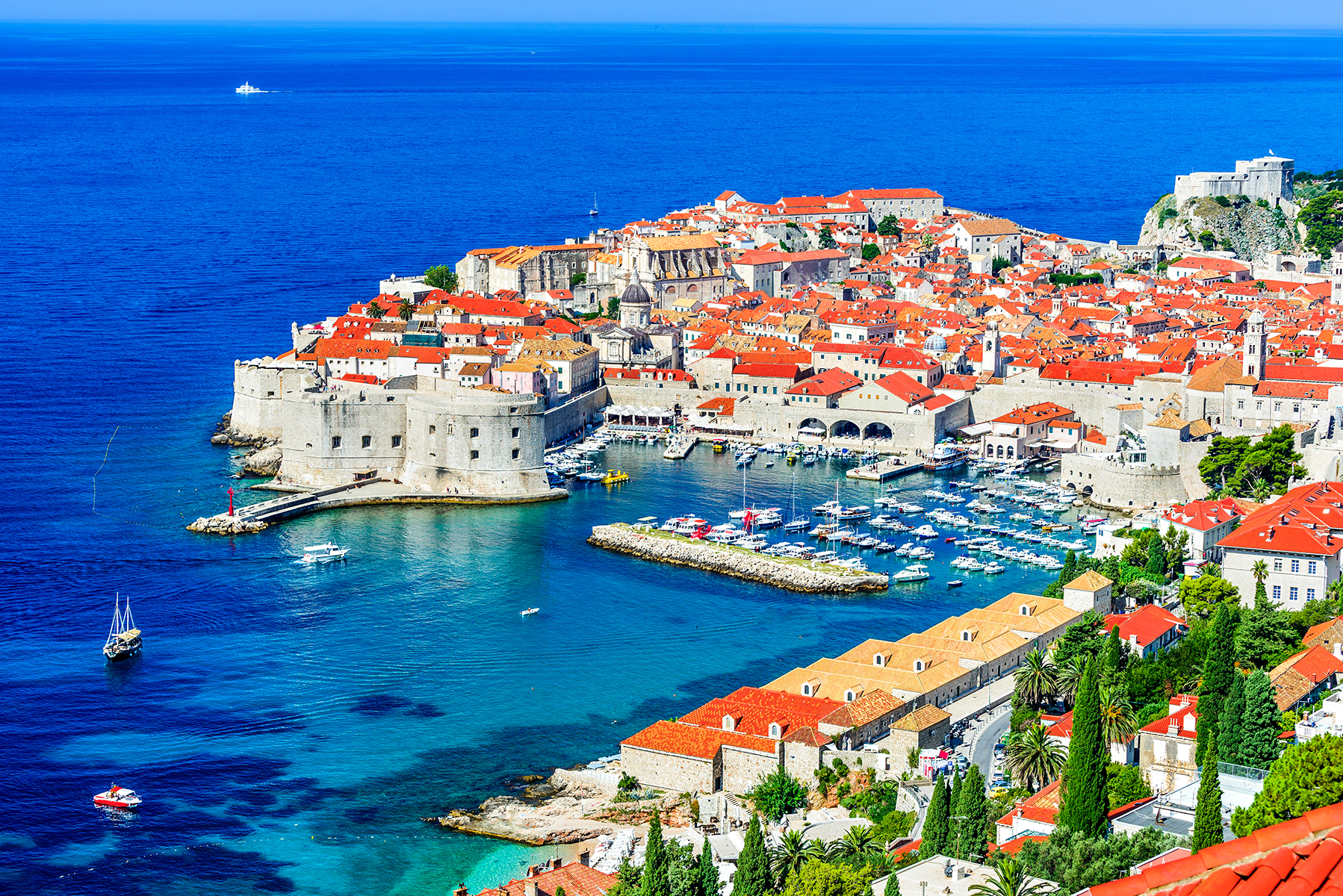 Blue body of water surrounding a town of clay-roofed houses, with a boat filled harbor in the middle.