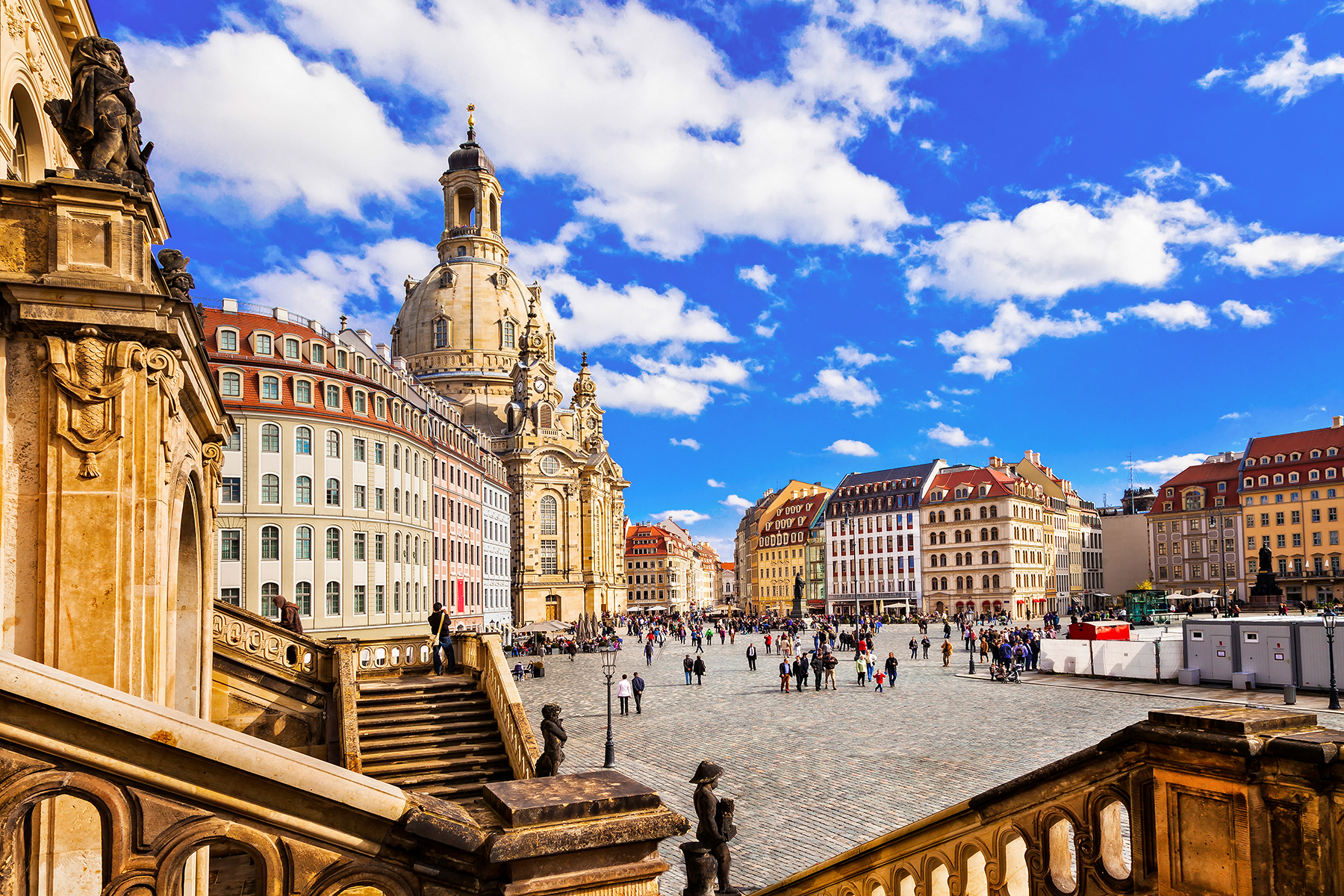 A town square in Dresden, with large old buildings surrounding a cobblestone street with people wandering around. 