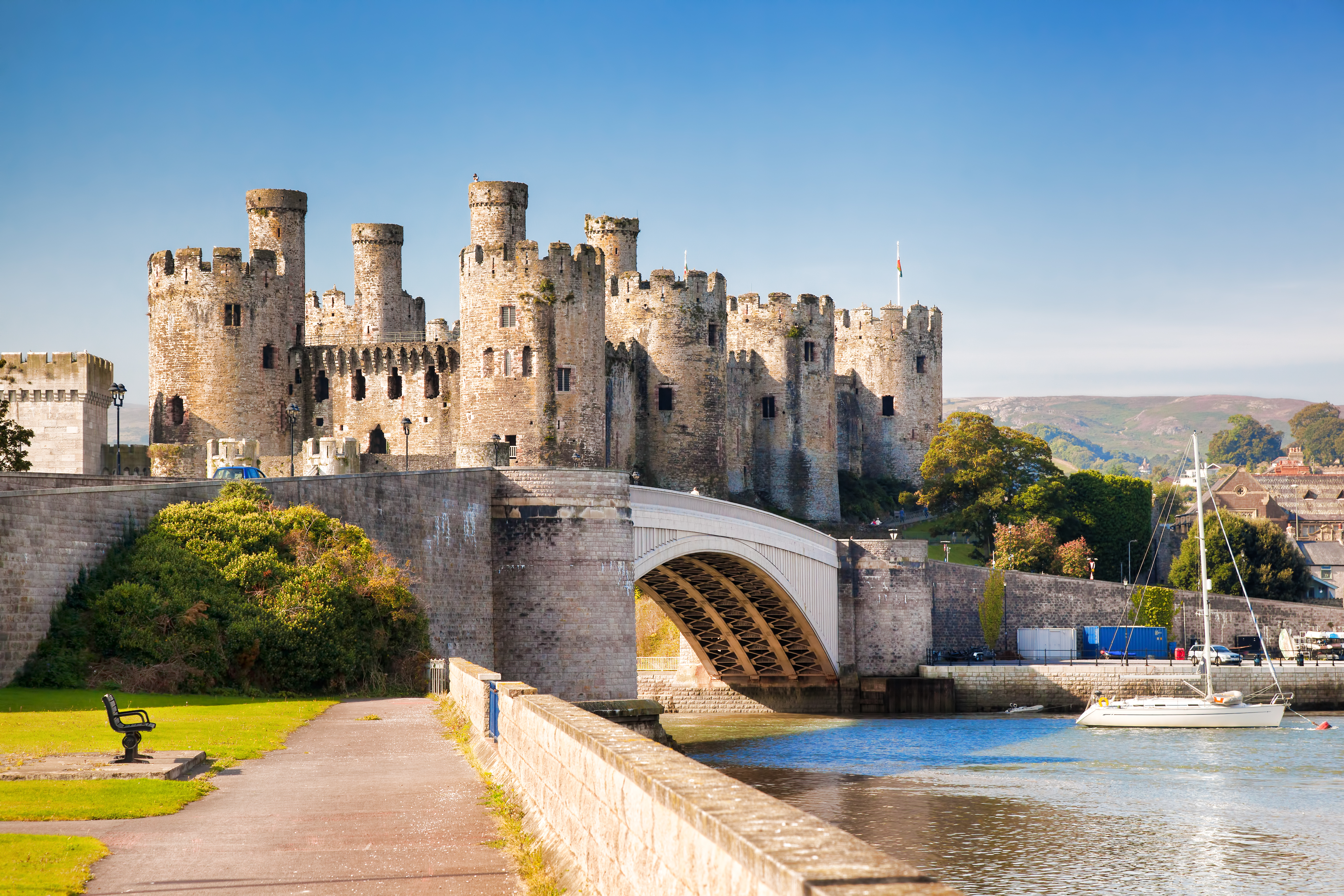 A large castle set above a river with a bridge and boats in the water. 