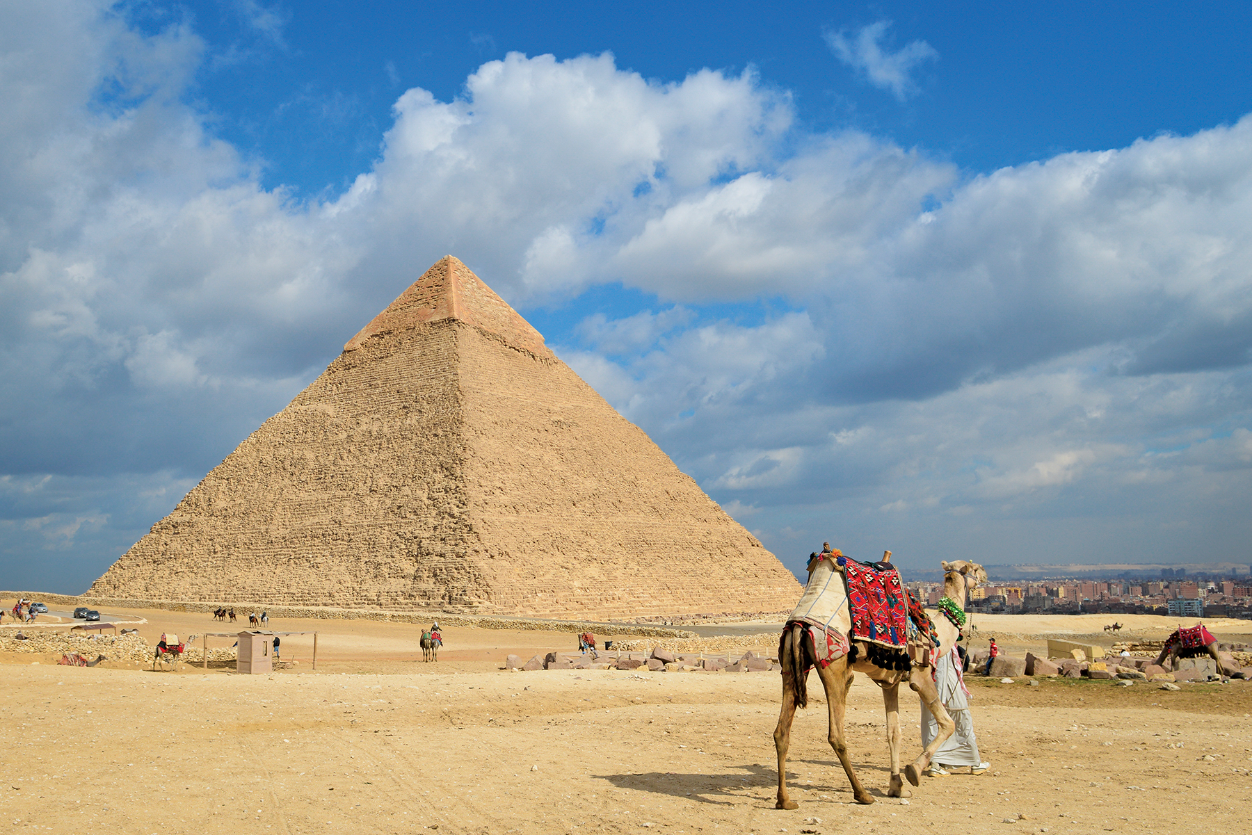 Picture of a pyramid in Egypt, with a person leading a camel into the desert. 