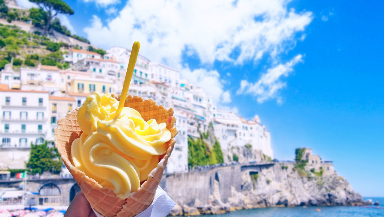 Hand holding gelato in a cone in front of Amalfi coast