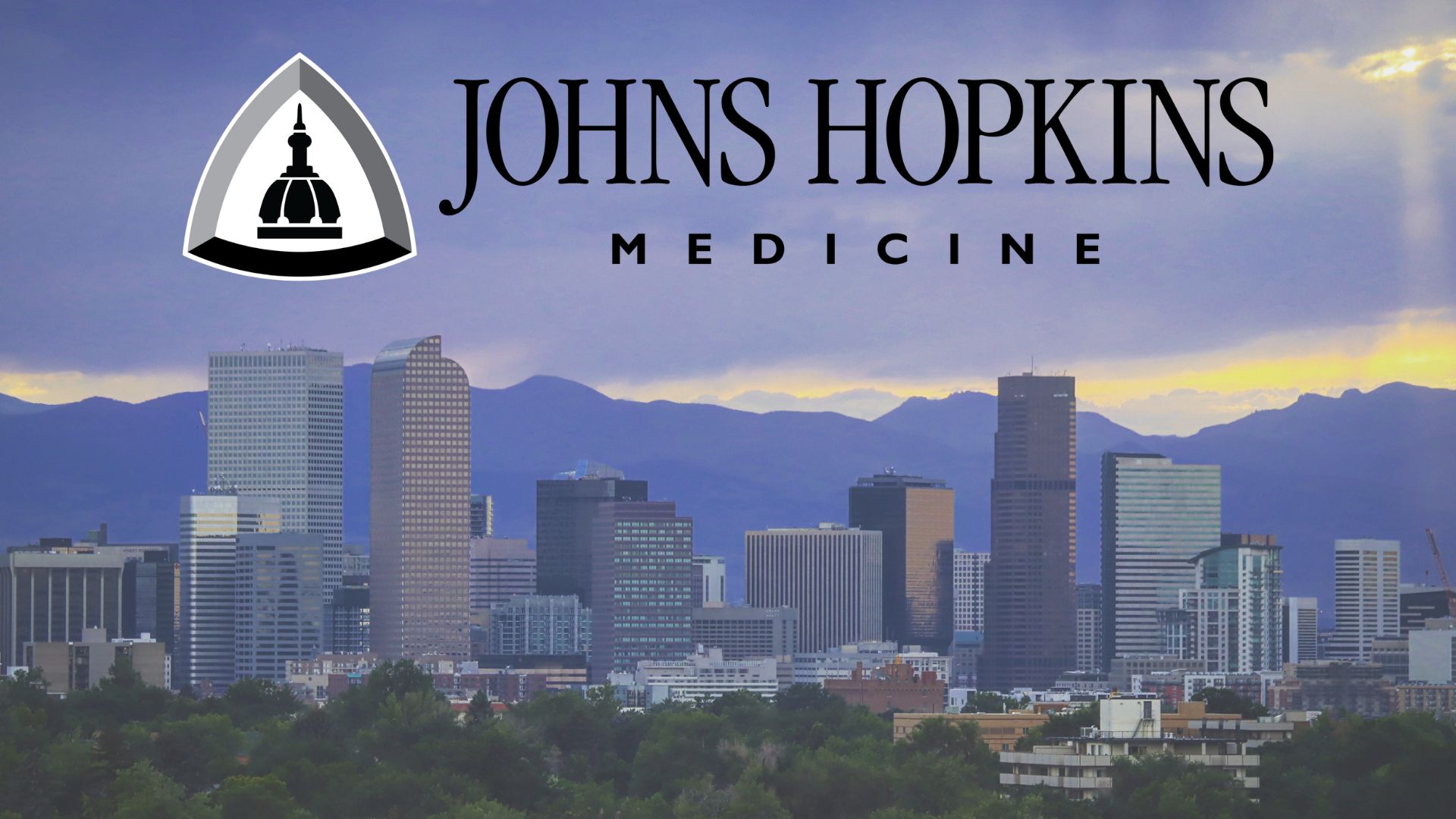 Downtown Denver with Mountains in the Background and the JHU SOM Logo