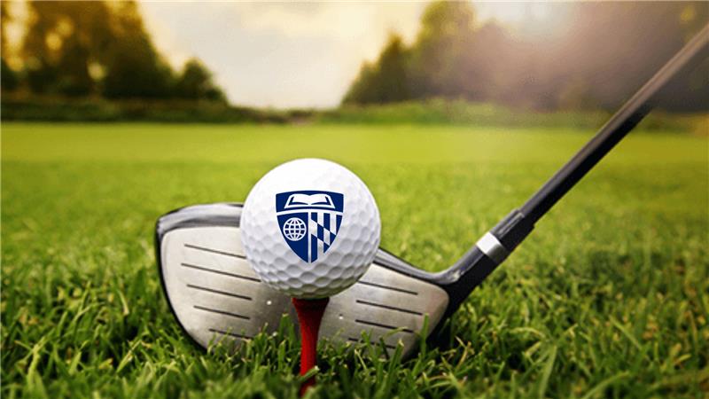 golf ball with golf club on green at sunrise, ball has Hopkins shield