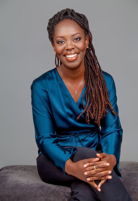 Michele Harper, author of The Beauty in Breaking, sits facing the viewer with her legs crossed, smiling, hands interlocked on her knees, facing the viewer. 