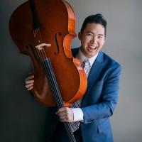 Taka Ariga Headshot. He has a blue blazer with white shirt. And he is carrying a cello with a big smile in this image.